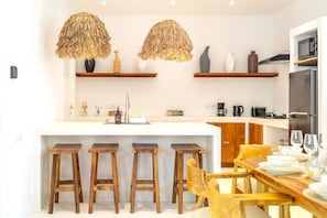 A modern kitchen with a central island, wooden stools, and hanging pendant lights. - Casa Myla by Betterplace (Pecatu)