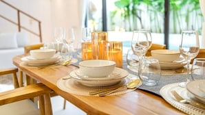 A dining table set with white plates, bowls, and glasses, with a view of greenery outside. - Casa Myla by Betterplace (Pecatu)