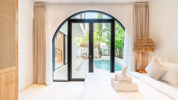 A modern bedroom with a large bed, a view of a swimming pool, and a glass door leading to an outdoor area. - Casa Myla by Betterplace (Pecatu)