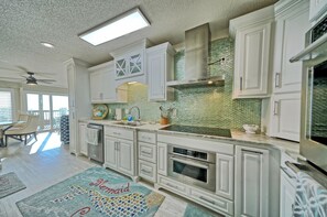 A spacious kitchen with white cabinetry, a large island, and a green mosaic backsplash. - Newly Renovated Beachfront 2BR Condo in Panama City Beach w/ Gulf Views & Balcony (Panama City)