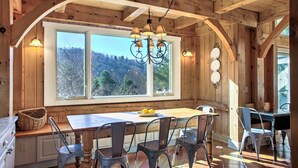A wooden interior with a large window, a chandelier, and a dining table with chairs. - Twin Timbers at the Falls | 2 Luxury Homes, Exclusive Pool, 13BR Retreat (Fairview)