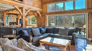 A spacious living area with a large leather sectional sofa, a wooden coffee table, and a dining table. There are multiple windows providing natural light and views of the outdoors. - Twin Timbers at the Falls | 2 Luxury Homes, Exclusive Pool, 13BR Retreat (Fairview)