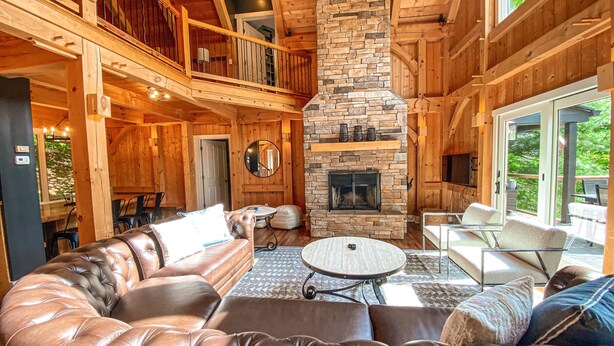 A cozy cabin interior with a stone fireplace, leather seating, and a balcony. - Twin Timbers at the Falls | 2 Luxury Homes, Exclusive Pool, 13BR Retreat (Fairview)