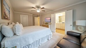 Ein Schlafzimmer mit einem großen Bett, einem Deckenventilator, einem Fernseher und einem durchgehenden Türrahmen einsehbaren Badezimmer.