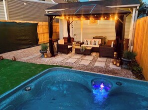 A backyard with a hot tub, patio furniture, and string lights.