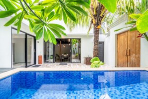 Ein moderner Poolbereich mit einem blauen, gefliesten Pool, umgeben von üppiger Vegetation und einer Holztür.