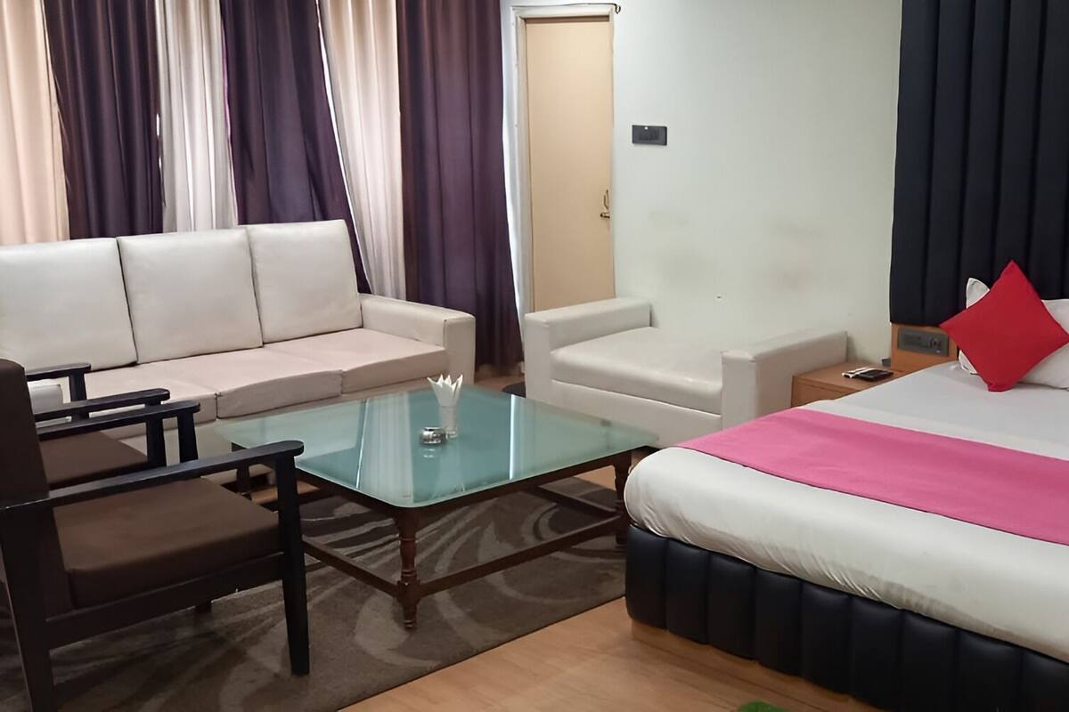 A hotel room with a bed, a sofa, a glass coffee table, and a nightstand.
