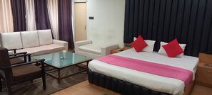 A hotel room with a bed, a sofa, a glass coffee table, and a nightstand. - Hotel Parbati International (Asansol)