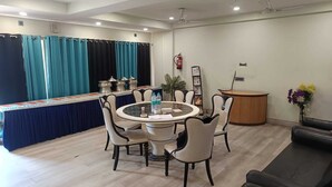 Une chambre d’hôtel comprenant une table de salle à manger ronde, quatre chaises, un comptoir de réception, un extincteur et une plante.