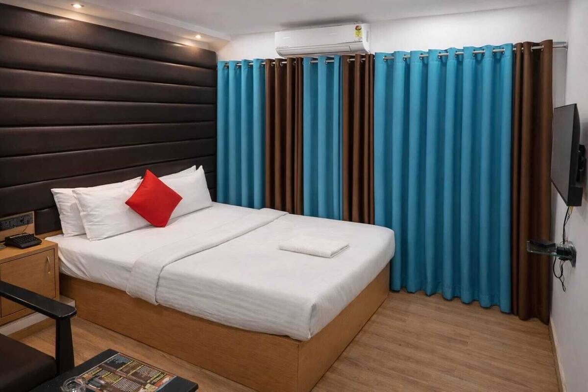 A hotel room with a bed, a nightstand, a TV, and a window with curtains.