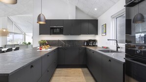 A modern kitchen with dark cabinetry, a large island, and a built-in oven. - VillaVilla 916 - Skåstrup Strand, Fyn og øer (Bogense)