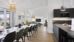 Cozinha moderna com uma ilha grande, área de jantar com uma mesa comprida e cadeiras, e sala de estar com sofá e televisão.