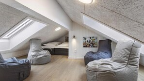 Un dormitorio tipo loft con techo inclinado, tragaluces, una cama, un escritorio y pufs.