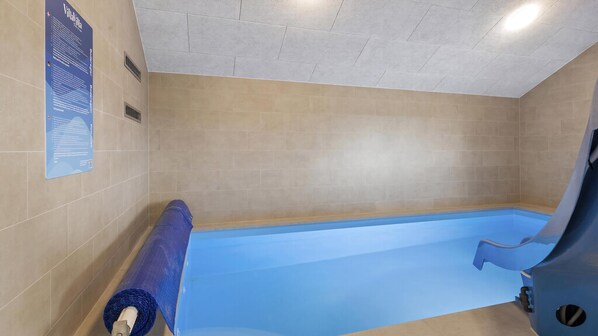 Una piscina con revestimiento azul, paredes de azulejos color beige e iluminación empotrada en el techo.