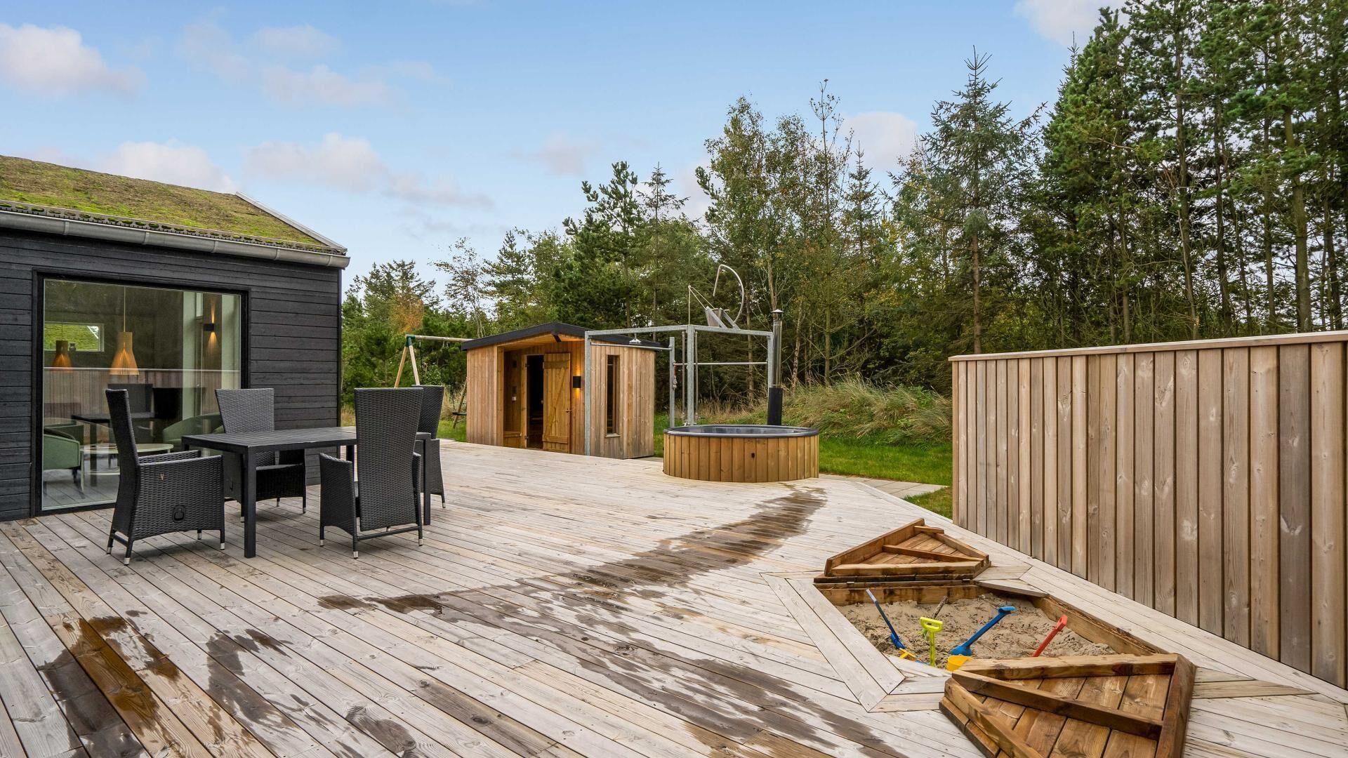 Een houten terras met buitenmeubilair, een bubbelbad en een houten speelgedeelte.