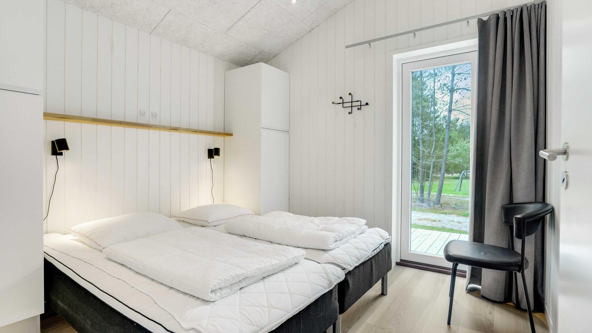 A modern bedroom with two beds, a small desk, and a view of a garden through a sliding door.