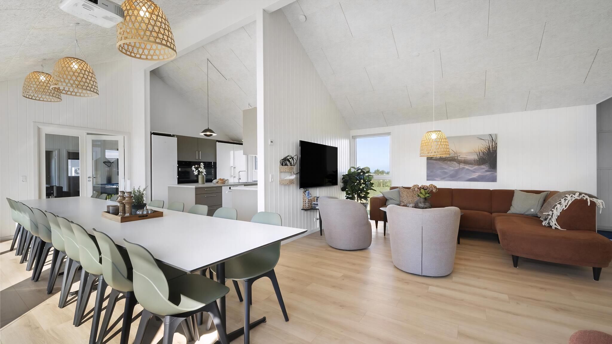 A spacious living area with a large dining table, a sofa, and a TV mounted on the wall.