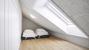 Ein kleiner Raum mit schrägem Dach, einem Oberlicht, Holzboden und einem Bett mit Kissen.