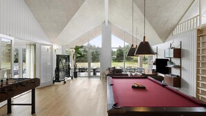 Una habitación amplia con mesa de billar, mesa de futbolín y un ventanal con vistas al exterior.