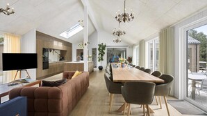 Un espacio habitable amplio con una larga mesa de comedor, asientos cómodos, una cocina y un ventanal grande.
