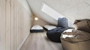 A loft bedroom with a sloped ceiling, wooden walls, and a skylight. There are two beds and a bean bag chair. - VillaVilla 933 - Østersøbadet, Lolland/Falster/Møn (Rødby)