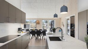 A modern kitchen with a central island, a dining area with chairs, and a view of the outdoors. - VillaVilla 933 - Østersøbadet, Lolland/Falster/Møn (Rødby)