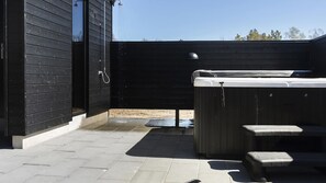 Eine Terrassenanlage mit Whirlpool, Holzdeck und einem schwarzen Gebäude.