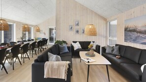 Ein modernes Wohnzimmer mit Essbereich, mit Holzwandverkleidung, schwarzen Sofas und Pendelleuchten.