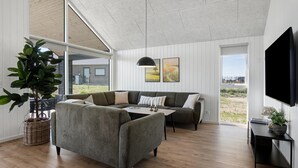 A modern living room with a sectional sofa, a coffee table, a large potted plant, and a flat-screen TV mounted on the wall. - VillaVilla 921 - Skåstrup Strand, Fyn og øer (Bogense)