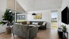 A modern living room with a sectional sofa, a coffee table, a large potted plant, and a flat-screen TV mounted on the wall. - VillaVilla 921 - Skåstrup Strand, Fyn og øer (Bogense)