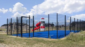 A fenced sports facility with a basketball court, a red slide, and a small building. - VillaVilla 921 - Skåstrup Strand, Fyn og øer (Bogense)