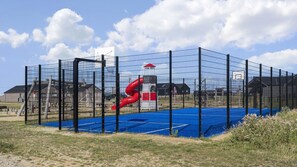 A fenced sports facility with a basketball court, a red slide, and a small building. - VillaVilla 921 - Skåstrup Strand, Fyn og øer (Bogense)