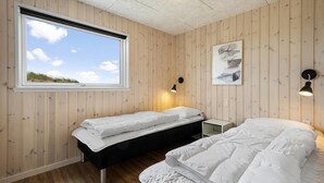 Una habitación con dos camas, una ventana y una lámpara fijada a la pared.
