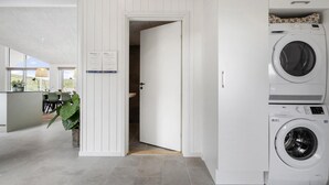 Un cuarto de lavado con lavadora y secadora de carga frontal, una puerta que da a otra habitación y vistas a un comedor con mesa y sillas.