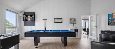 A pool table in a room with white paneled walls, a dartboard, and a framed picture.