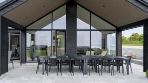 A covered outdoor dining area with a table and chairs, large windows, and a view of the landscape. - VillaVilla 922 - Faaborg, Fyn og øer (Faaborg)