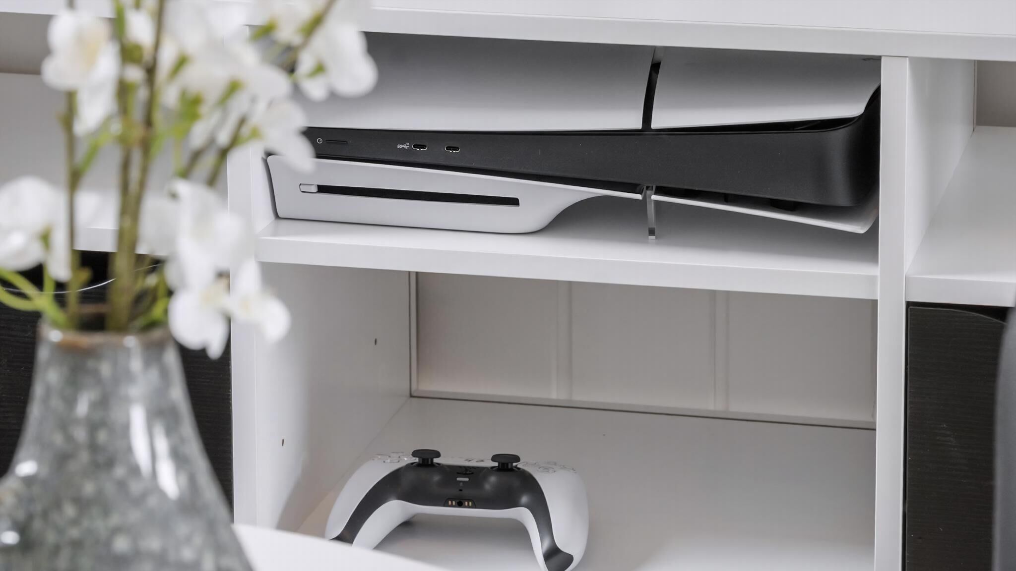 En hvid hylde med en spillekonsol og en controller.