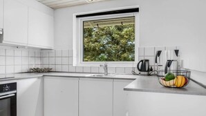 Et moderne køkken med hvide skabe, en rustfri stålvask, en elkedel og en skål med frugt på bordet.