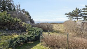 Paisaje natural con valla de madera, follaje denso y vista al mar.