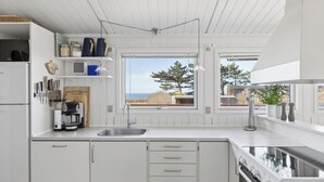 Una cocina moderna con armarios blancos, estufa integrada, un fregadero y un ventanal con vistas al exterior.