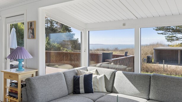 Una sala de estar moderna con un sofá gris, una mesita con una lámpara y ventanas amplias que ofrecen vistas al exterior.