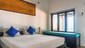 Une chambre d’hôtel avec un lit, un banc, une fenêtre et une lampe fixée au mur.