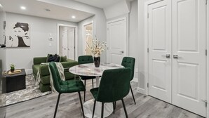 A modern living room with a green sofa, a round table, and a vase of flowers. There are white doors and a black side table. - 2BR Basement Suite + Sofa Bed | Near Airport (Calgary)