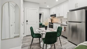 A modern kitchen with white cabinets, a stainless steel refrigerator, and a marble dining table with green chairs. - 2BR Basement Suite + Sofa Bed | Near Airport (Calgary)