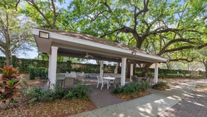 A covered outdoor patio with tables and chairs, surrounded by greenery and trees. - Thematic 4 bdr House Near Disney - 11-105lv (Kissimmee)