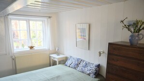 A bedroom with a bed, a dresser, a nightstand, a window with curtains, a radiator, and a framed picture on the wall.