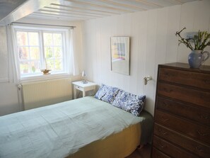 A bedroom with a bed, a dresser, a nightstand, a window with curtains, a radiator, and a framed picture on the wall. - Historic townhouse in the heart of Ærøskøbing. (Ærøskøbing)
