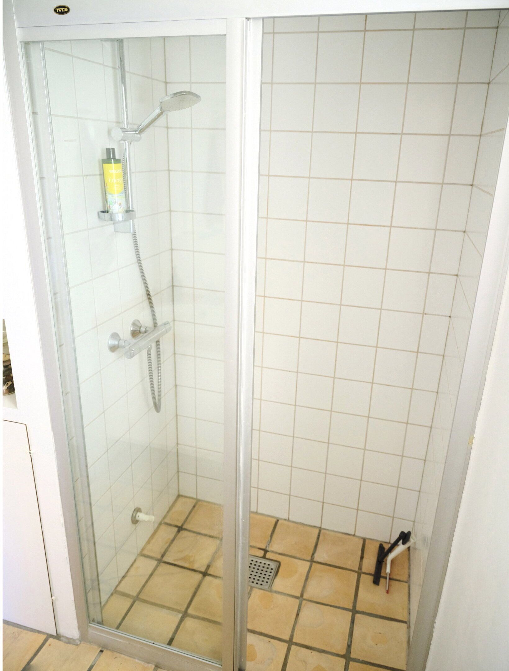 Une douche fermée par des parois en verre, dotée d’un pommeau de douche à main et d’un robinet à main.