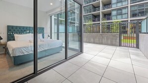 Une chambre d’hôtel moderne avec un grand lit, un mur en verre et une vue sur un immeuble à plusieurs étages.