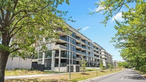 Un immeuble moderne à plusieurs étages, doté de balcons, entouré d’arbres et surplombant un ciel dégagé.